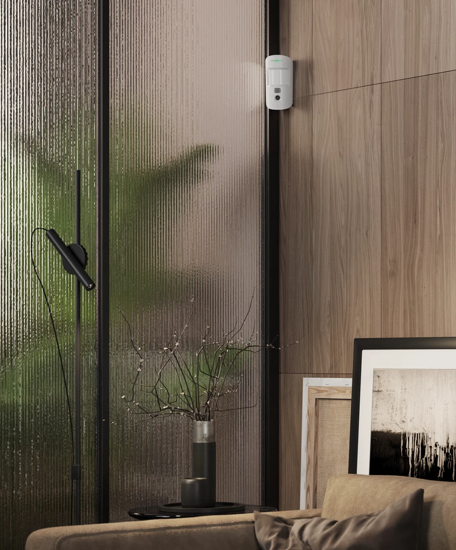 White Ajax MotionCam mounted beside a glass door in a modern home interior